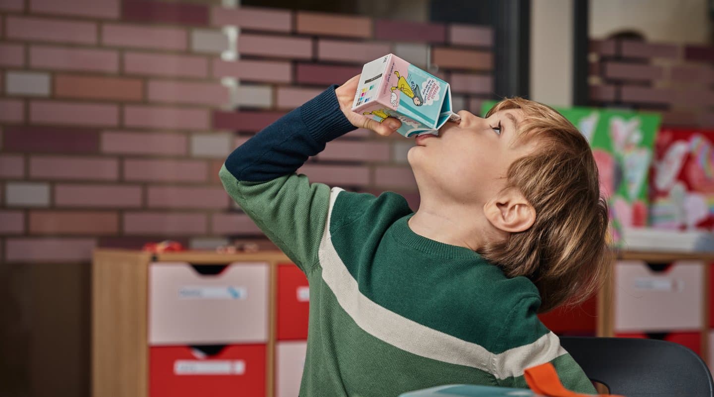 Et barn sitter i et klasserom og drikker melk fra en kartong.